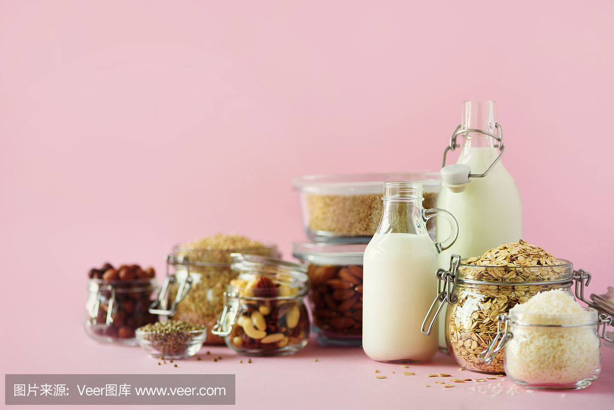 素食代替牛奶。玻璃瓶与非乳制品的牛奶和原料在粉红色的背景与复制空间。清洁饮食,无乳制品,素食,防过敏,健康的食品理念